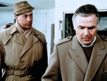 Copyright: Filmverleih Zwei Männer in Mänteln stehen nebeneinander in einem Raum, einer mit Hut, beide mit nachdenklichem Ausdruck.