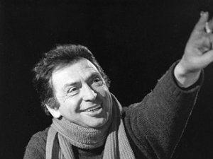 Copyright: Filmverleih
Alfred Vohrer mit Schal lächelt und streckt eine Hand nach oben, Schwarz-Weiß-Aufnahme vor dunklem Hintergrund.