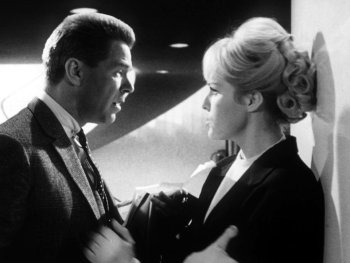 Copyright: Filmverleih Schwarzweißfoto einer Filmszene mit einem Mann im Anzug und einer Frau mit hochgestecktem Haar, die sich in angespanntem Gespräch gegenüberstehen.