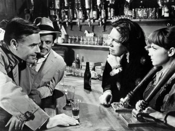Copyright: Filmverleih Schwarz-weiß Filmszene an einer Bartheke mit vier Personen im Gespräch, im Hintergrund zahlreiche Flaschen und Gläser auf Regalen.
