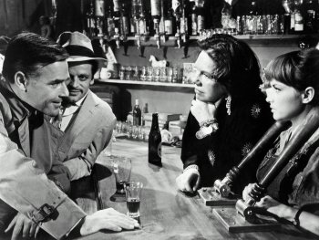 Copyright: Filmverleih Schwarz-weiß Filmszene an einer Bartheke mit vier Personen im Gespräch, im Hintergrund zahlreiche Flaschen und Gläser auf Regalen.