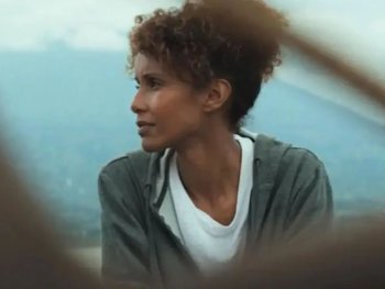 Copyright: Filmverleih Person mit lockigem Haar blickt zur Seite, im Hintergrund eine hügelige Landschaft im Dunst.