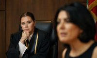 Eine Richterin in Robe sitzt nachdenklich im Gerichtssaal, während im Vordergrund unscharf eine weitere Person zu sehen ist.