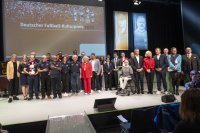Große Gruppe von Personen steht auf einer Bühne vor einer Leinwand mit der Aufschrift „Deutscher Fußball-Kulturpreis 2025“.