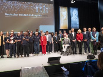Große Gruppe von Personen steht auf einer Bühne vor einer Leinwand mit der Aufschrift „Deutscher Fußball-Kulturpreis 2025“.