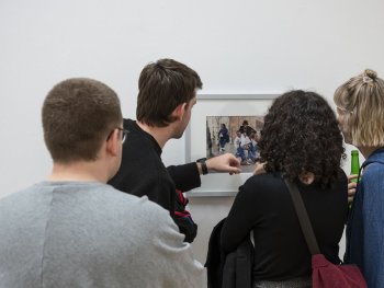 Foto: Rebecca Schwarzmeier
Vier Personen betrachten von hinten ein gerahmtes Foto einer Personengruppe an einer weißen Wand, eine Person zeigt dabei auf das Bild.