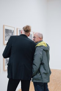Zwei Personen betrachten im Gespräch gerahmte Schwarz-Weiß-Fotografien an einer Galeriewand.