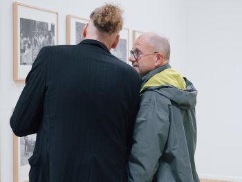 Zwei Personen betrachten im Gespräch gerahmte Schwarz-Weiß-Fotografien an einer Galeriewand.