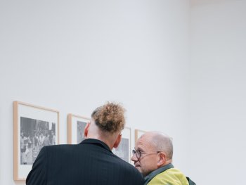 Foto: Laura Michele Kniesel
Zwei Personen betrachten im Gespräch gerahmte Schwarz-Weiß-Fotografien an einer Galeriewand.