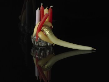 Copyright: Andreas Oehlert, Stagebeauty (7), Detail, 2010, Pigmentdruck auf Papier, 54 x 41 cm Mehrere bunte Kerzen in einem Glashalter sind teilweise geschmolzen und verbogen, gespiegelt auf schwarzem Untergrund vor dunklem Hintergrund.