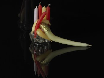 Copyright: Andreas Oehlert, Stagebeauty (7), Detail, 2010, Pigmentdruck auf Papier, 54 x 41 cm Fotografie zeigt mehrere farbige Kerzen stecken in einem Glashalter, wobei einige davon geschmolzen und verbogen über den Rand hängen, vor schwarzem Hintergrund mit spiegelnder Oberfläche.