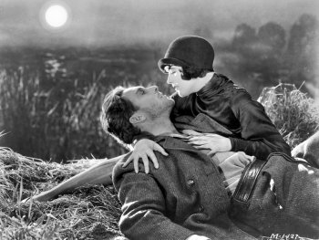 Copyright: San Francisco Film Preserve Schwarz-Weiß-Filmszene, in der ein Mann im Gras liegt und eine Frau mit Hut ihm nahe an das Gesicht gebeugt ist, im Hintergrund Schilf und Mond.