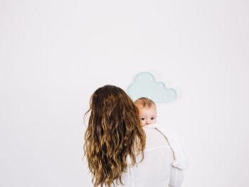 Copyright: freepik.com Eine Person trägt ein Baby auf der Schulter, das über die Schulter blickt, im Hintergrund hängt eine wolkenförmige Dekoration an der Wand.