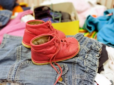 Ein Paar rote Kinderschuhe liegt auf einer Jeansjacke inmitten eines Haufens gebrauchter Kleidungsstücke.