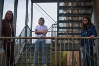 Monteith: Drei Personen mit langen Haaren stehen auf einer Außentreppe aus Metall und blicken in die Kamera.