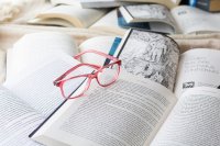 Eine rosa Brille liegt auf einem aufgeschlagenen Buch inmitten mehrerer geöffneter Bücher mit bedruckten Seiten.
