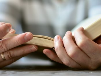 Zwei Hände blättern in Nahaufnahme in einem aufgeschlagenen Buch.