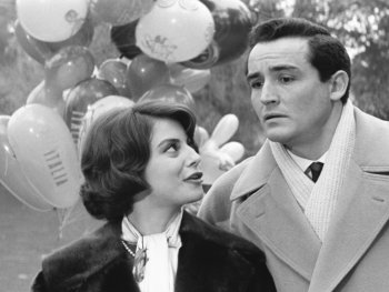 Copyright: Filmverleih Schwarz-weißes Filmstandbild mit einem Paar in Wintermänteln vor Luftballons, im Hintergrund eine Frau mit Kind.