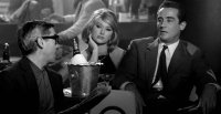 Schwarz-Weiß-Filmszene mit zwei Männern in Anzügen und einer Frau an einem Tisch mit Champagnerkühler in einer Bar.