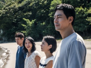 Copyright: Netflix Services Germany GmbH Vier Personen stehen hintereinander gestaffelt an einem Sandstrand vor bewaldeten Hügeln und blicken in die gleiche Richtung.