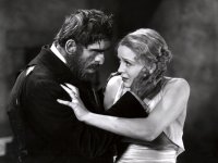 Schwarz-weiße Filmszene, in der ein bärtiger Mann eine Frau im Abendkleid bedrängt, während sie den Kopf abwendet und ihn mit der Hand auf Abstand hält.