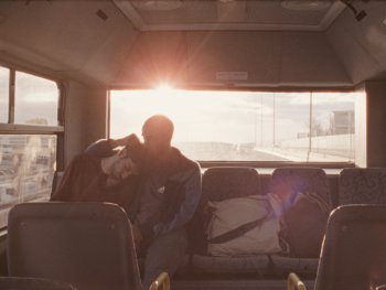 Copyright: INSIDE OUT FILMS, NAKBA FILMWORKS 2024 Person sitzt im Gegenlicht der untergehenden Sonne in einem Bus und blickt aus der Fensterfront nach draußen.