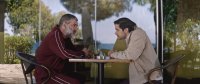 Zwei Männer sitzen sich an einem Tisch in einem Café im Freien gegenüber und führen ein ernstes Gespräch.
