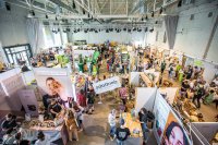 Gut besuchte Messe in einer hohen Industriehalle mit vielen Ständen für vegane und nachhaltige Produkte, zwischen denen Besucherinnen und Besucher entlangschlendern.