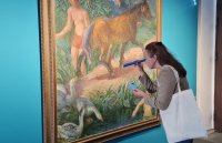 Eine Person mit Stofftasche betrachtet in einer Ausstellung durch eine blaue Rolle ein großes Gemälde mit Pferd, Gänsen und badenden Menschen.