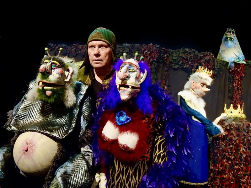 Two human-sized, animalistic puppets, representing a royal couple. They are controlled by a puppeteer behind them, looking straight ahead in concentration.