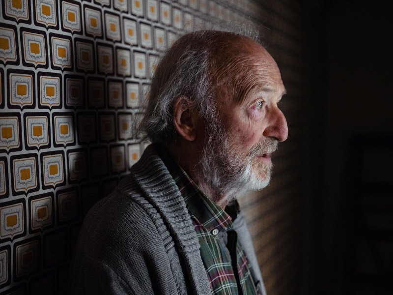 Close-up of an old man leaning against a wall, looking seriously into the distance.