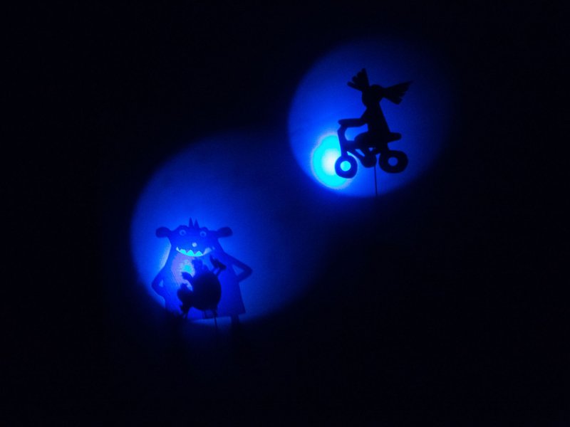 A shadow play from two blue light cones showing a monster and a child riding a bicycle.