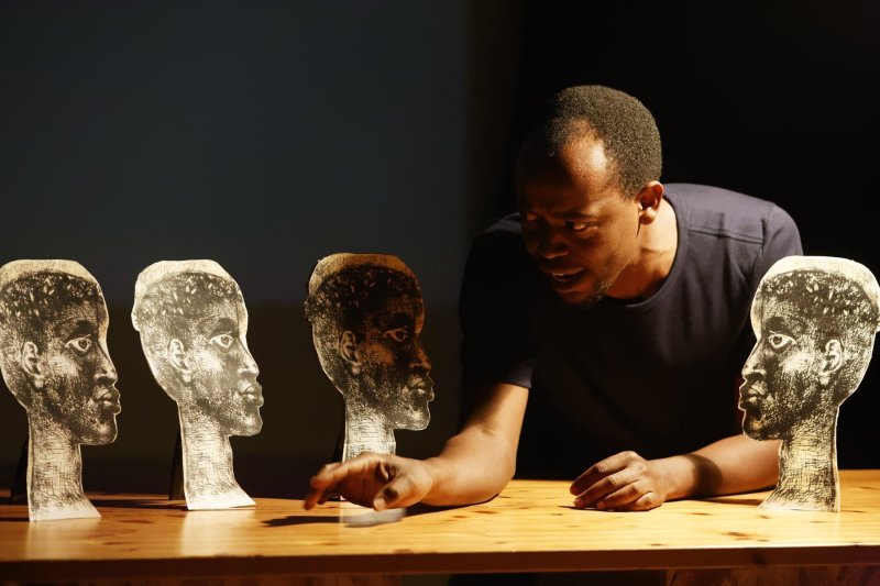 A person of colour is sitting at a table, talking to 4 paper silhouettes standing around him.