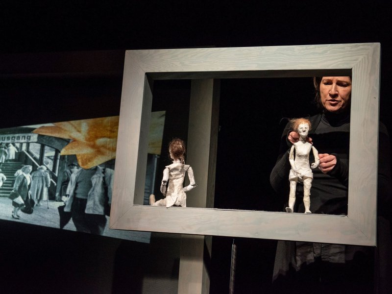 Photo of two small crafted female figures in a wooden frame being controlled by a puppeteer.