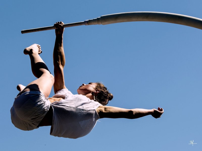 Eine Frau hält sich mit der rechten Hand akrobatisch an einer gebogenen Metallkonstruktion.