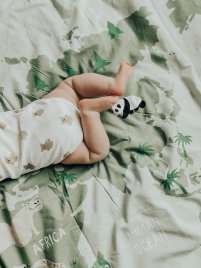 Die Beine eines Babys liegen angewinkelt auf einer Bettwäsche mit Weltkarten-Motiv und Tierdrucken wie Panda und Nilpferd.