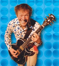 Kinderliedermacher Geraldino im gepunkteten Hemd mit Gitarre vor Retrotapete mit blauen Kreisen