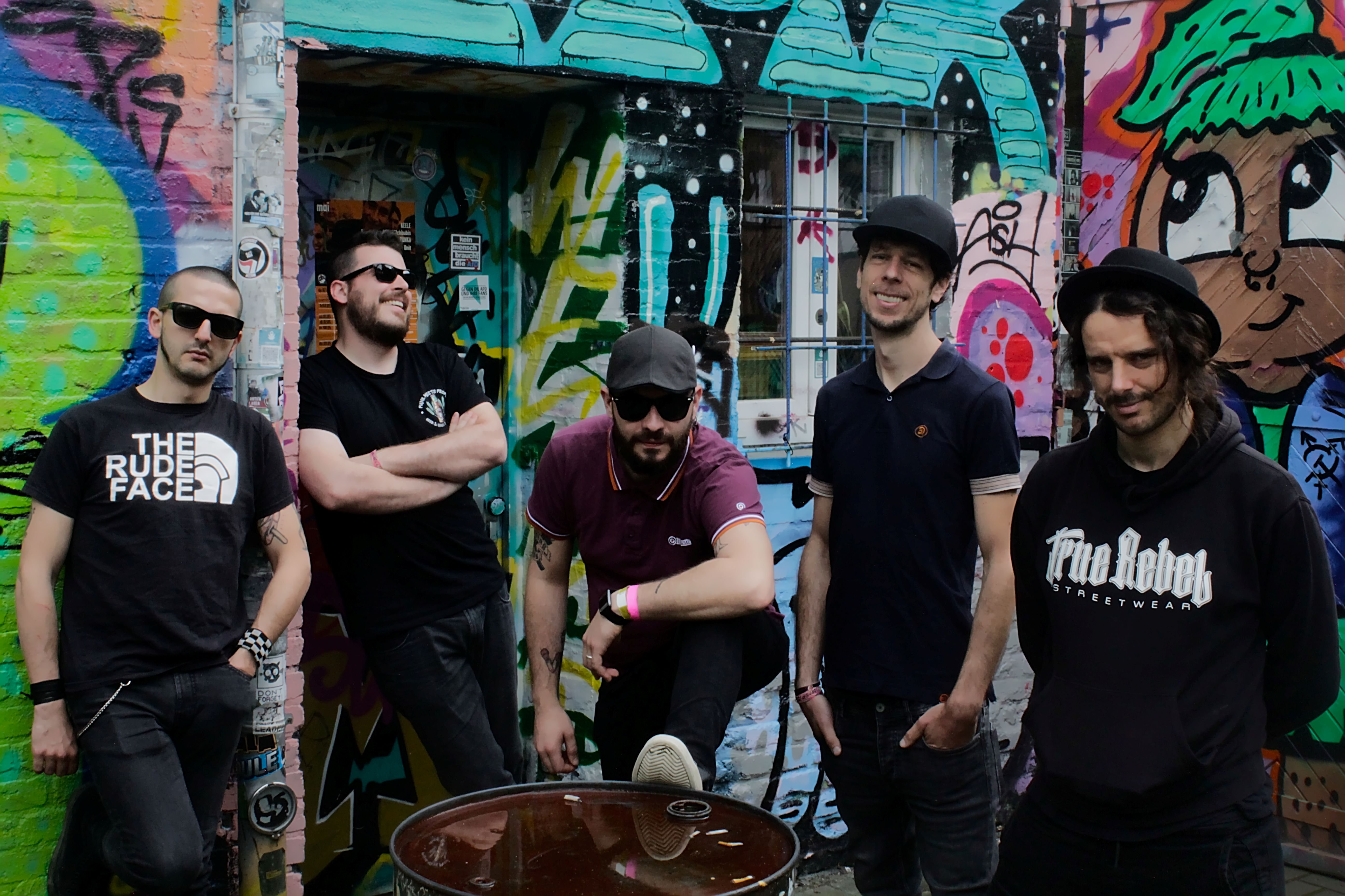 5 Männer stehen vor einer Wand, die mit Graffiti besprüht ist