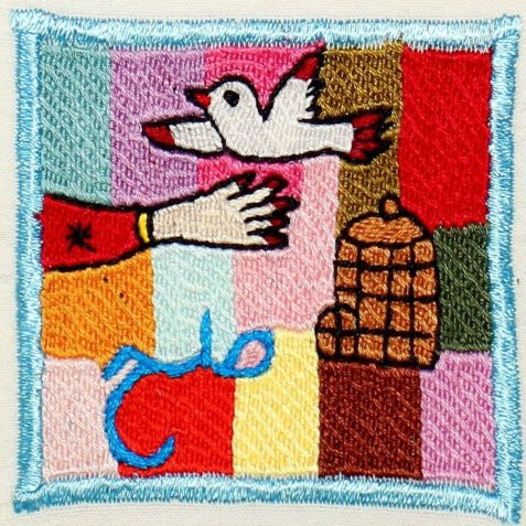 Stickerei mit einer weißen Taube, die über eine ausgestreckte Hand fliegt, neben einem braunen Vogelkäfig vor buntem Hintergrund.