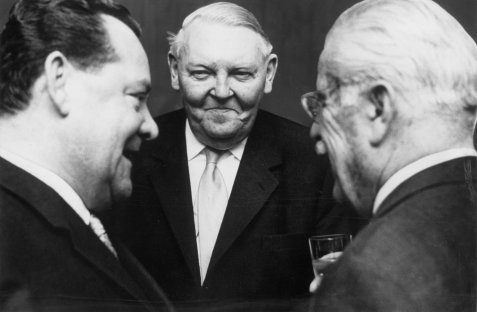 Schwarz-weiß-Aufnahme von Max Grundig, Ludwig Erhard und Gustav Schickedanz, die in einer Gesprächssituation stehen.