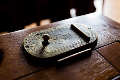 Nahaufnahme eines mit einem Kleeblatt verzierten, rechteckigen Messing-Tintenfasses mit Stempel und Federhalter auf einem Holztisch.