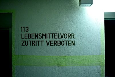 Schwarze Wandbeschriftung mit der Nummer '113' und dem Text 'LEBENSMITTELVORR. ZUTRITT VERBOTEN' auf einer hellen Wand im Kronacher Bunker.