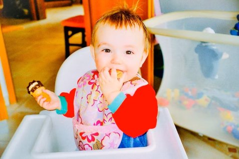 Kind sitzt im Hochstuhl und hält Essen in der Hand