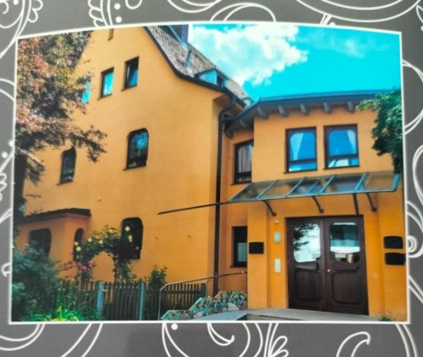 Das zweistöckige gelbe Gebäude des Waldorfkindergartens mit mehreren Fenstern und brauner Haustür unter blauem Himmel