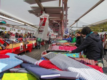 Marktstand mit bunten Stoffen und mehreren Personen im Hintergrund unter einem überdachten Marktbereich