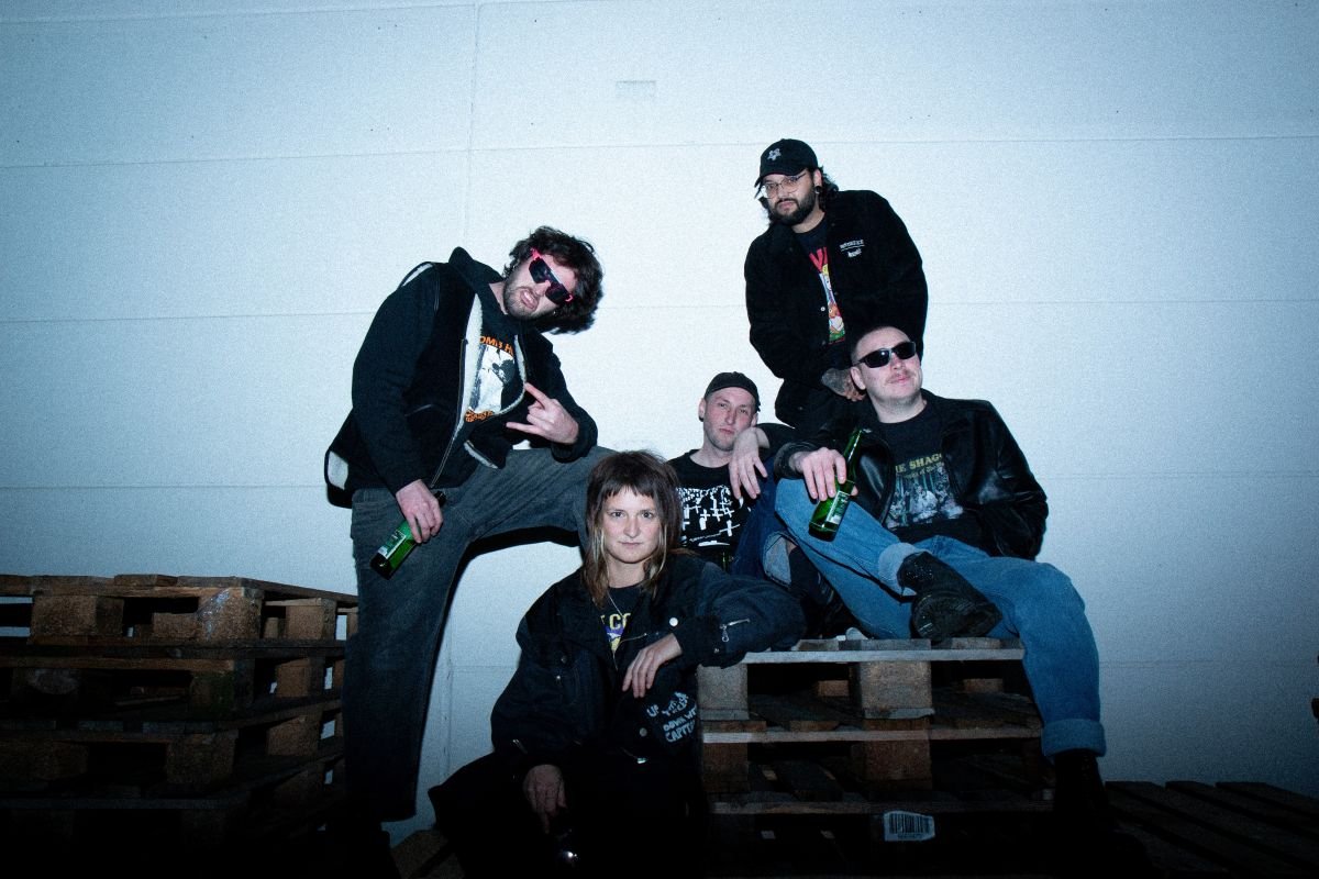 1 Frau und vier Männer sitzen auf Paletten vor einer Wand