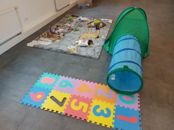 Kinderspielbereich mit buntem Zahlenpuzzle, grün-blauem Spielzelt und Spielzeug auf Teppich