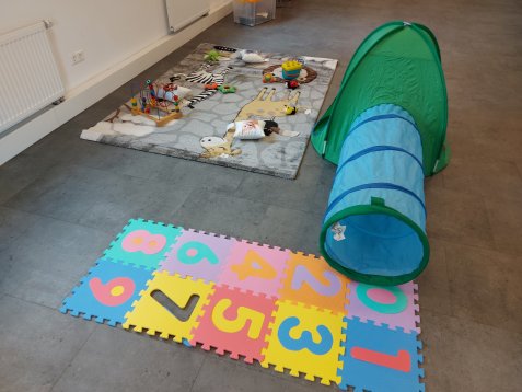 Kinderspielbereich mit buntem Zahlenpuzzle, grün-blauem Spielzelt und Spielzeug auf Teppich
