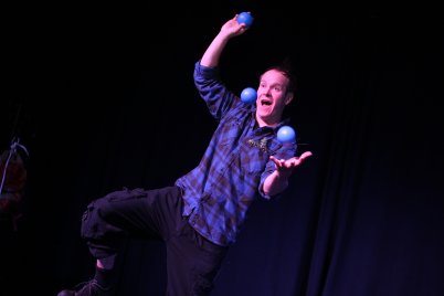 Hannes Hoffmann in kariertem Hemd jongliert mit mehreren blauen Bällen vor schwarzem Hintergrund