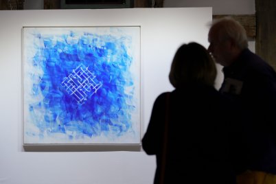 Zwei Menschen betrachten eine Kalligrafie Wolffs. Blau auf Papier, gerahmt.